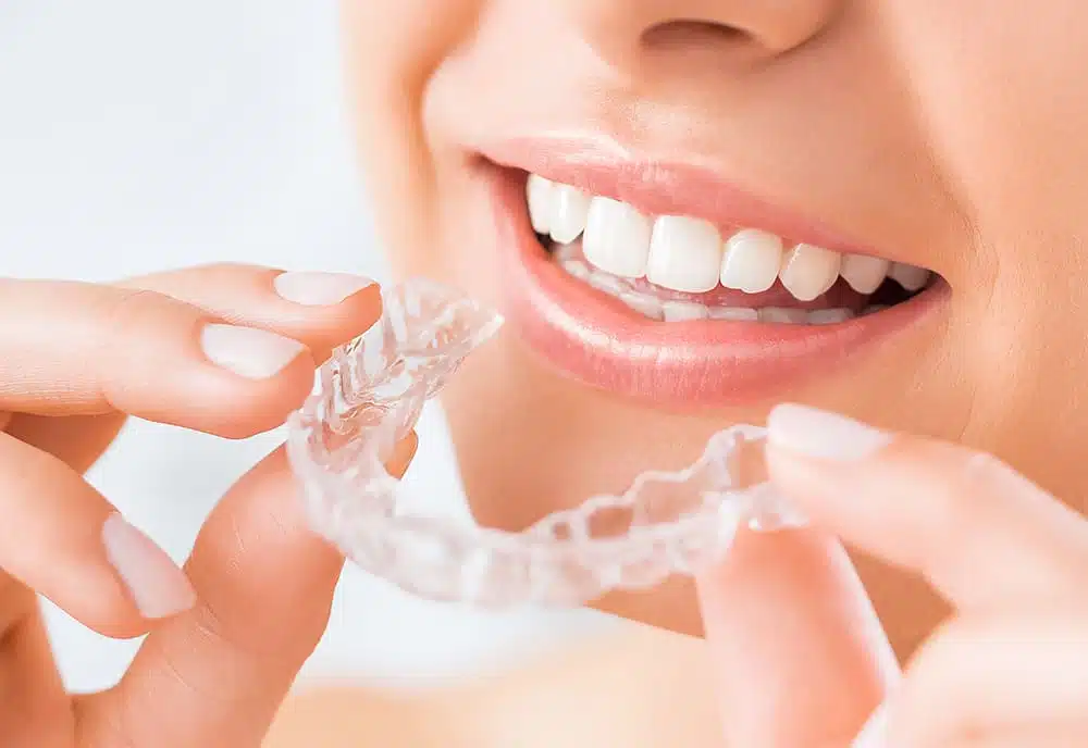 Woman holding a clear Invisalign aligner up to her smile